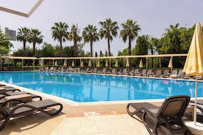 A swimming pool with lounge chairs and umbrellas, surrounded by palm trees.