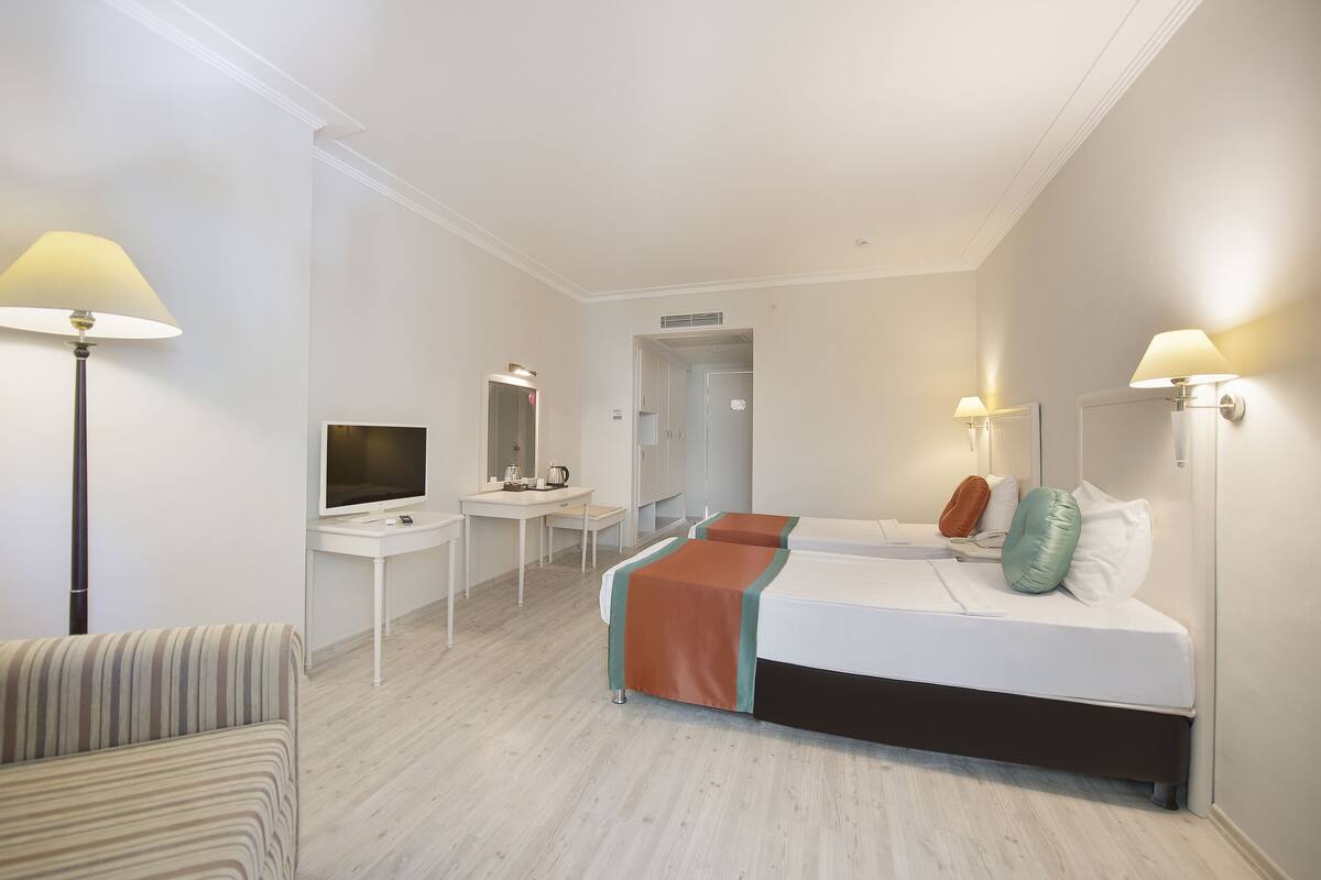 Una habitación de hotel con cama, mesitas de noche, escritorio, silla, televisor y lámpara.