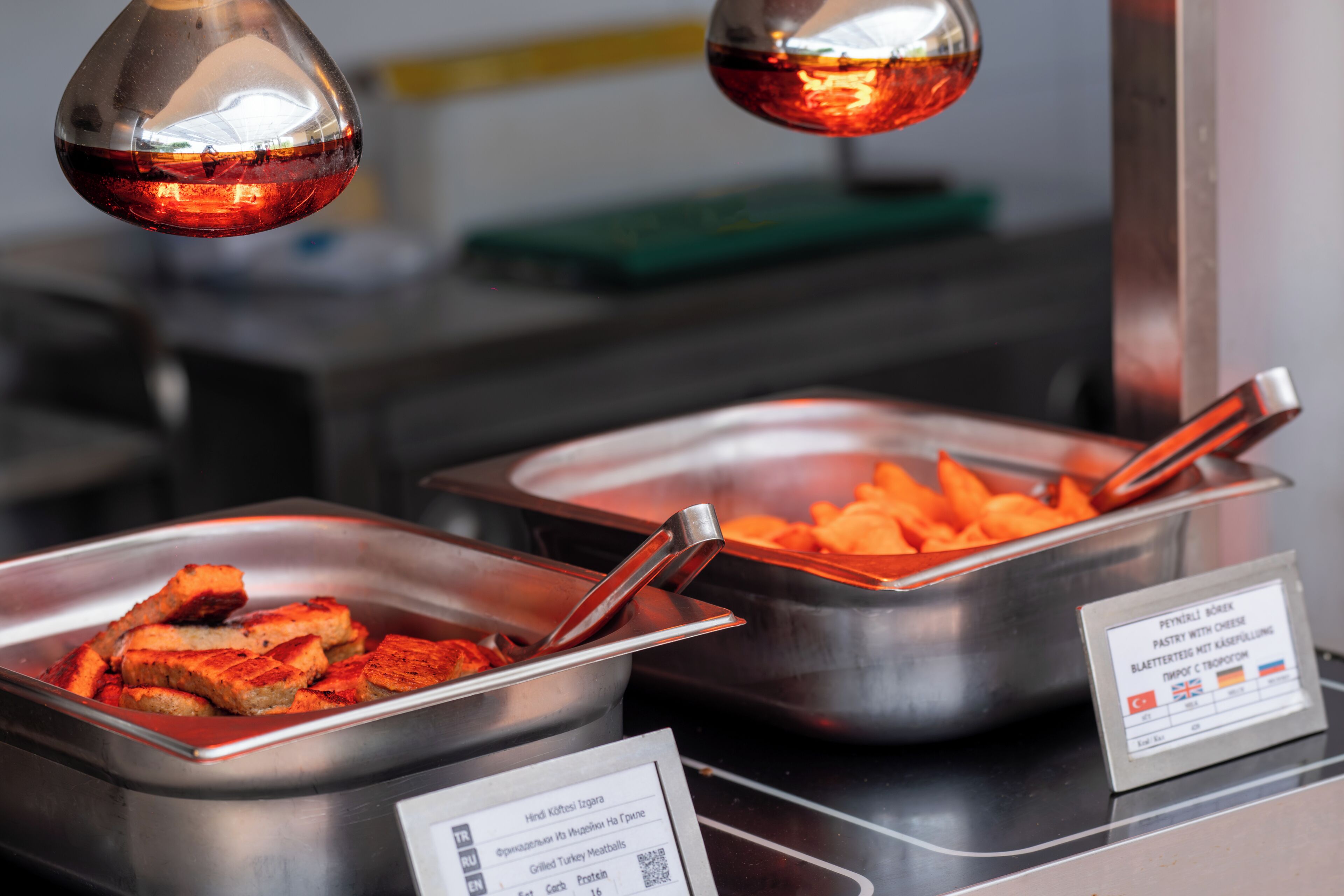 Ein Buffet mit verschiedenen Speisen, darunter gegrillte Hackbällchen vom Truthahn, und ein Schild, das die Verfügbarkeit unterschiedlicher Sprachen anzeigt.
