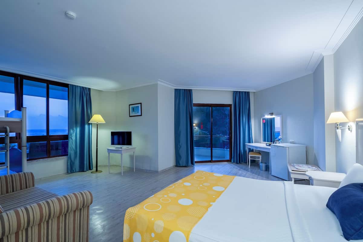 Habitación de hotel con cama, escritorio, silla, televisor y balcón con vistas.