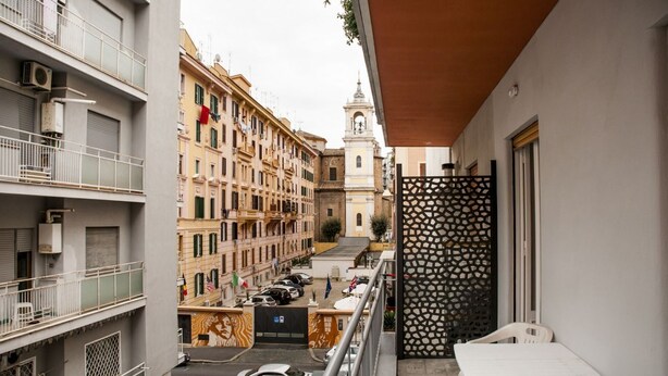 Un balcon donnant sur une rue, un bâtiment doté d’une tour horloge et une clôture décorative.