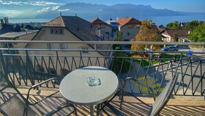 Un balcón con mesa y sillas, con vistas a un pueblo con casas y una cordillera.