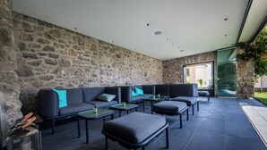 Un espacio moderno al aire libre con muros de piedra, suelo oscuro y una mezcla de sofás y mesas.