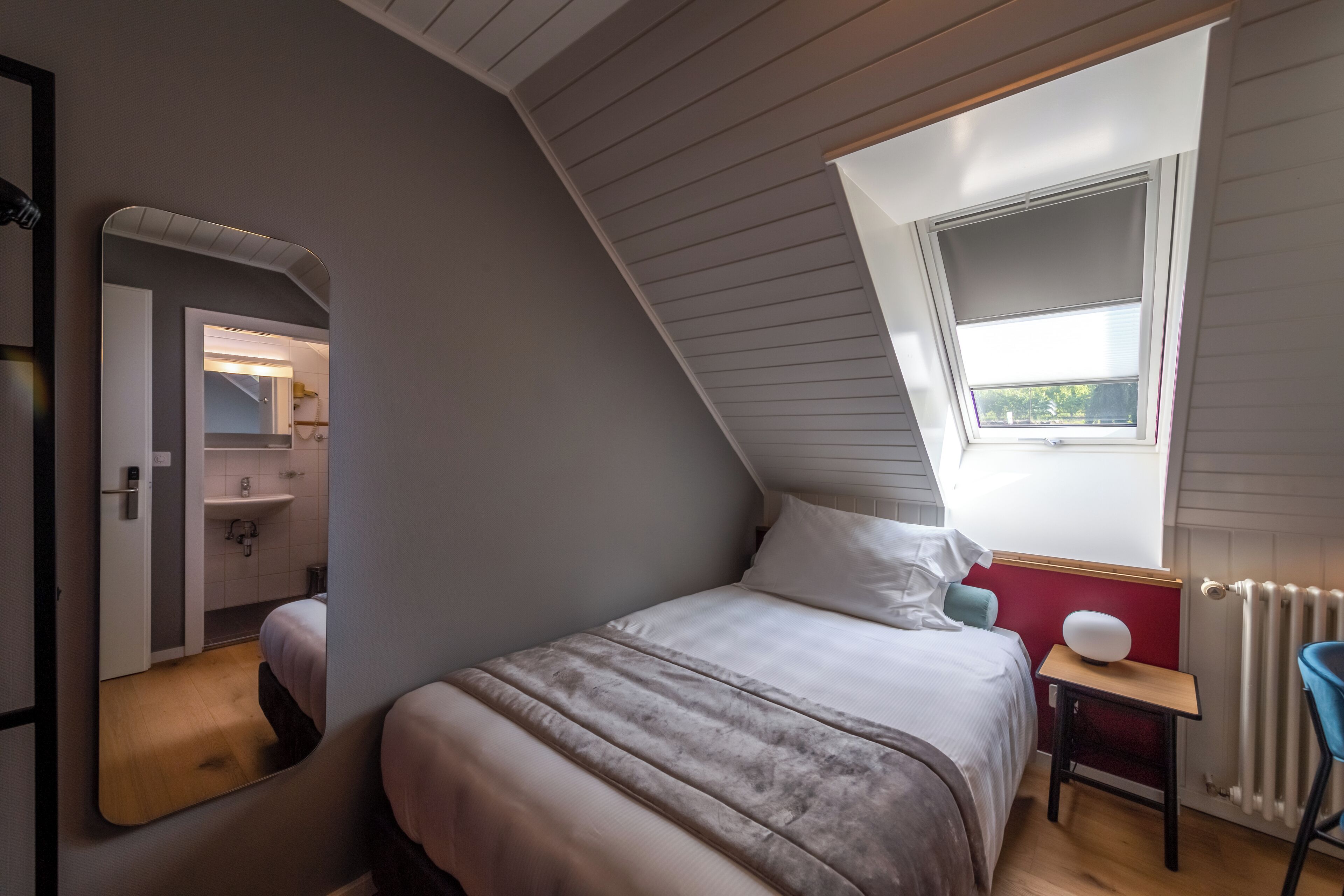 A bedroom with a sloped ceiling, a skylight, a bed, a bedside table, and a chair.