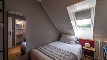A bedroom with a sloped ceiling, a skylight, a bed, a bedside table, and a chair.