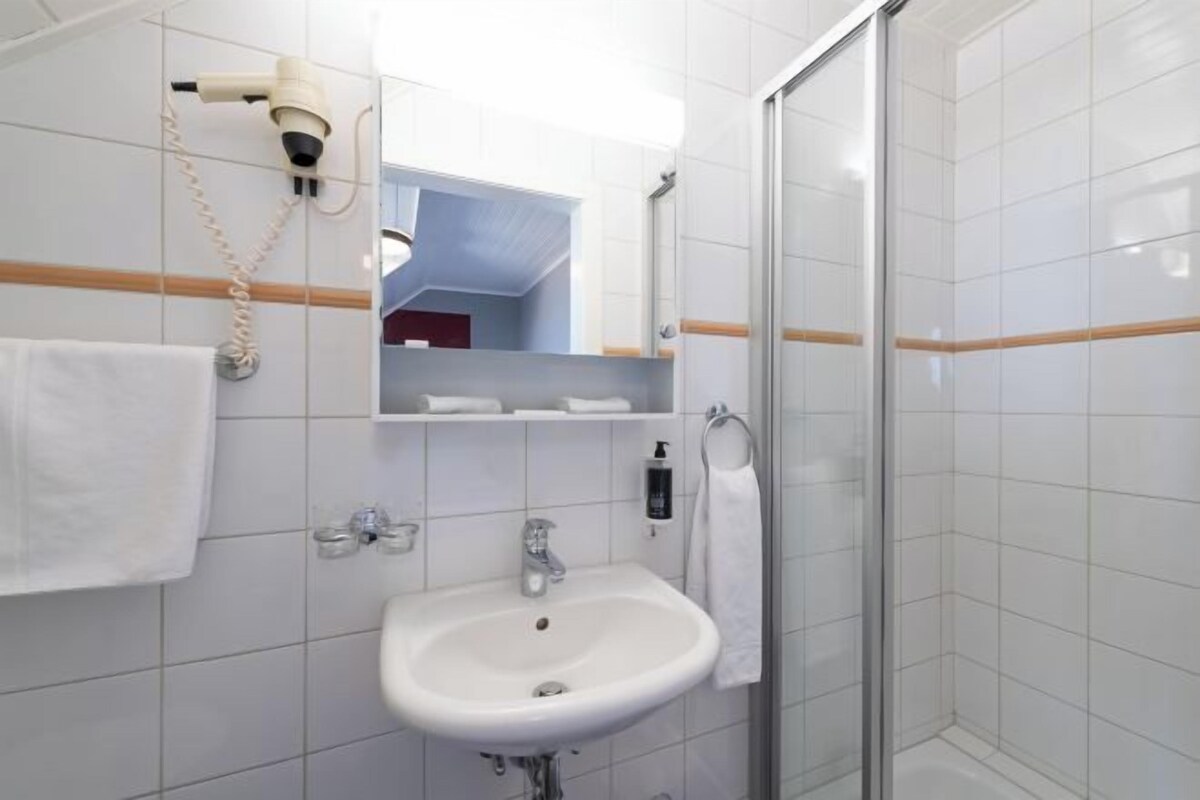Un baño con lavamanos blanco, un espejo, secador de pelo y cabina de ducha de vidrio.