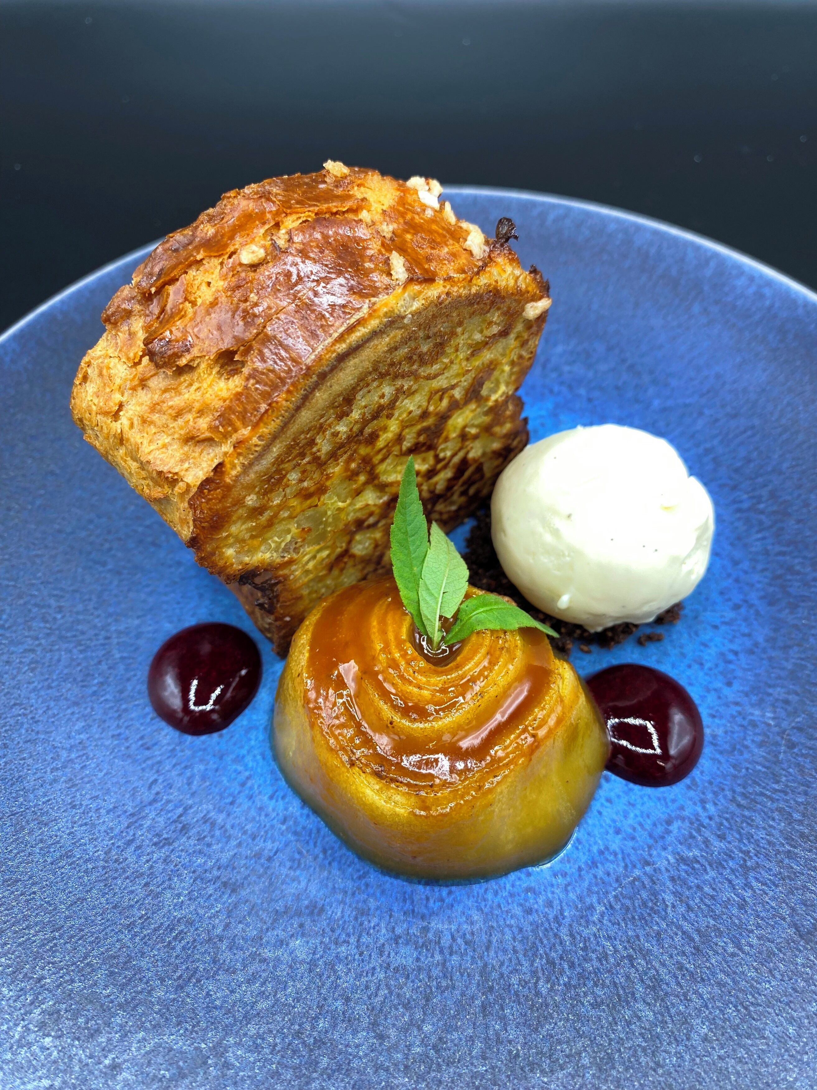 Un plato de postre con un flan de caramelo, un trozo de pan y una porción de helado.