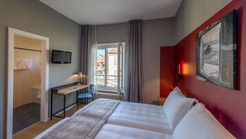 A hotel room with a bed, desk, chair, TV, and a window with curtains.