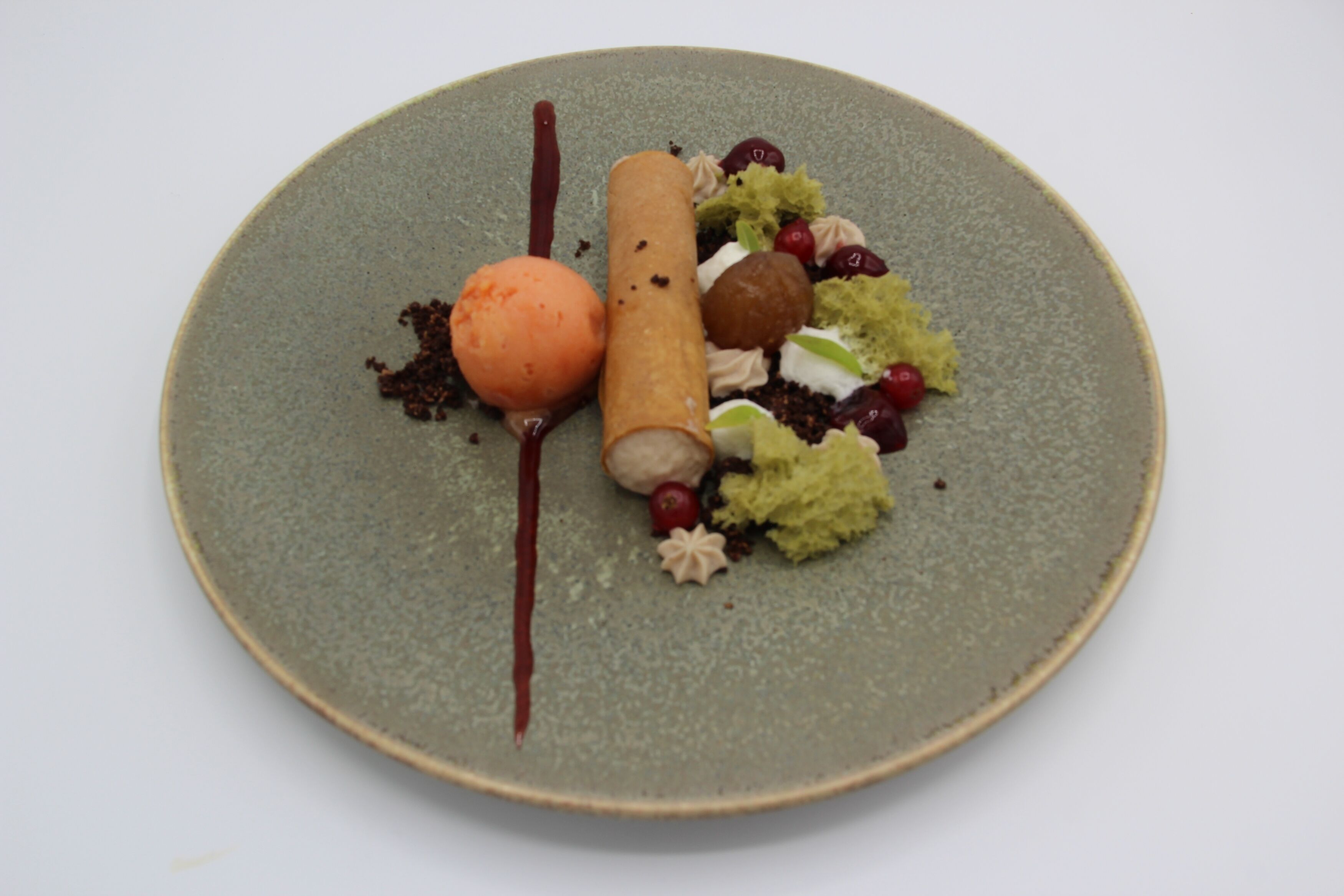 Un piatto dessert con diversi elementi, tra cui un cialda arrotolata, una pallina di gelato e frutta secca assortita.