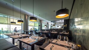 Un restaurante moderno con varias mesas, sillas negras e iluminación colgante.