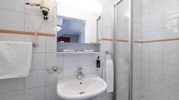 A bathroom with a white sink, a mirror, a hairdryer, and a glass shower enclosure.