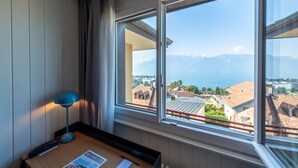 Habitación de hotel con un amplio ventanal que ofrece vistas al mar y a las montañas.