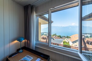 Quarto de hotel com uma janela grande que oferece vista para o mar e montanhas.