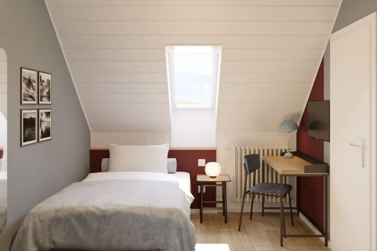 Un dormitorio con una cama, un escritorio, una silla, un radiador y una ventana.