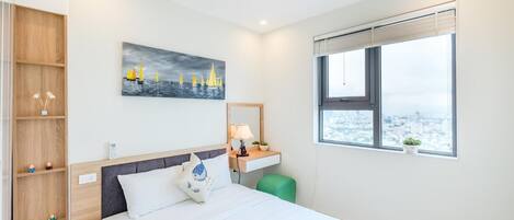 Een hotelkamer met een bed, nachtkastje, raam met uitzicht op de stad, houten garderobe en een schilderij aan de muur.