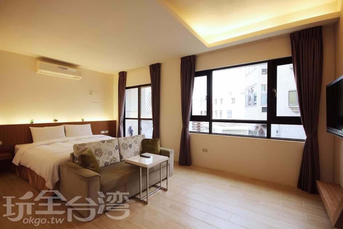 A hotel room with a bed, a sofa, a small table, and large windows with curtains.