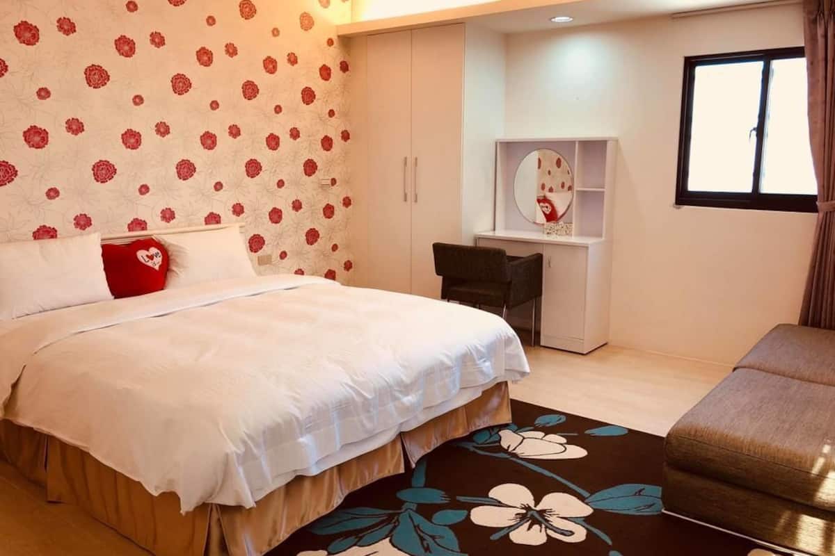 A bedroom with a bed, a desk, and a chair. There is a window with curtains.