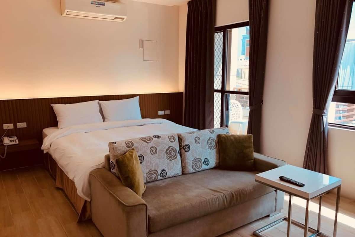 A hotel room with a bed, a sofa, a small table, and a window with curtains.