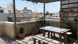 Une terrasse sur le toit, avec une table en bois et des bancs, entourée de plantes en pot et d’une pergola.