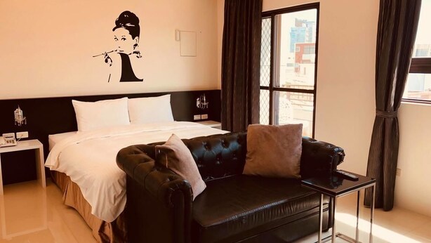 Une chambre d’hôtel avec un lit, un canapé en cuir noir, une petite table et une fenêtre avec des rideaux.