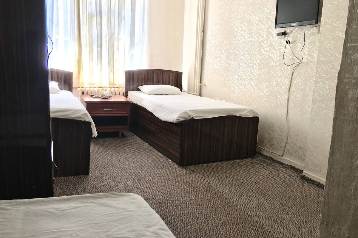 A hotel room with two single beds, a small desk with a telephone, and a television mounted on the wall.