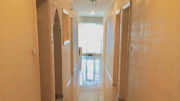 Un pasillo con pisos de baldosas y paredes lisas, que conduce a una habitación luminosa con una ventana.