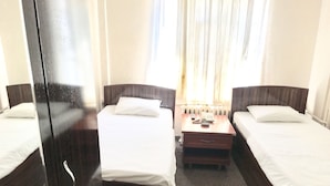 Habitación de hotel con dos camas individuales, una mesita de noche de madera y una ventana con cortinas.