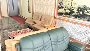 Un hall con una zona de estar que incluye dos sofás verdes y dos sillones beiges. Un tapiz con estampado cubre el suelo y un cuadro enmarcado adorna la pared.