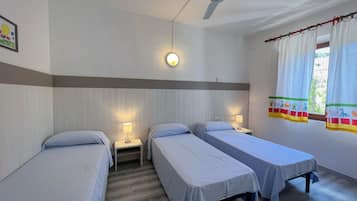 A room with three single beds, a ceiling fan, bedside lamps, and a window with curtains.