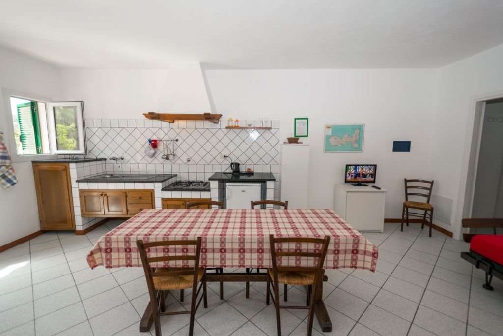 A compact kitchen with a dining area, featuring a checkered tablecloth, wooden chairs, and a tiled floor.