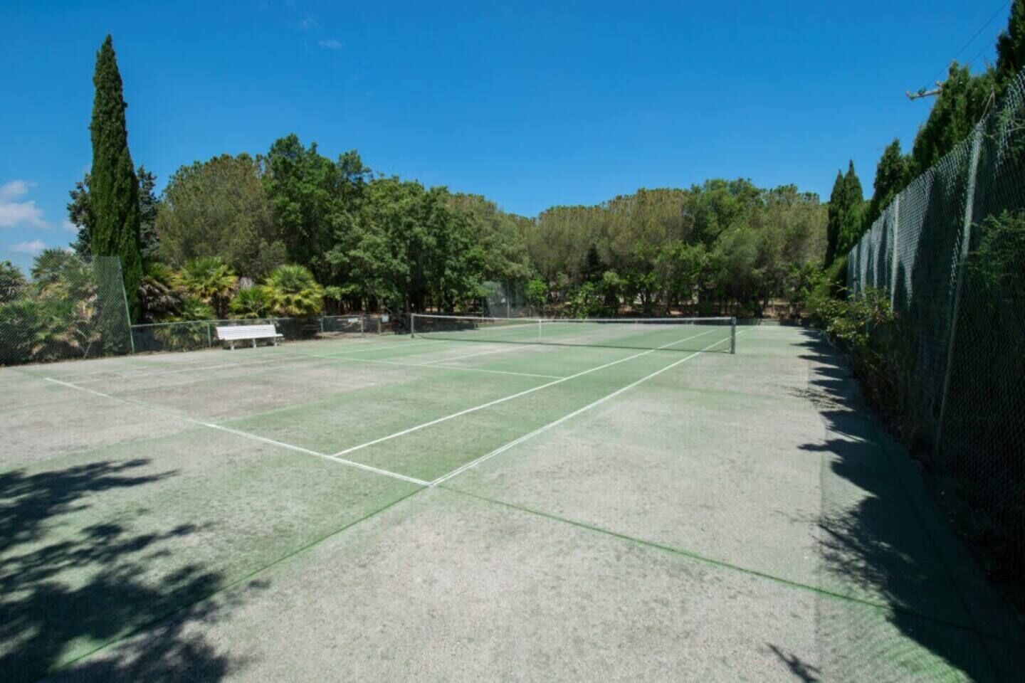 An outdoor tennis court with a net, surrounded by trees and a fence.