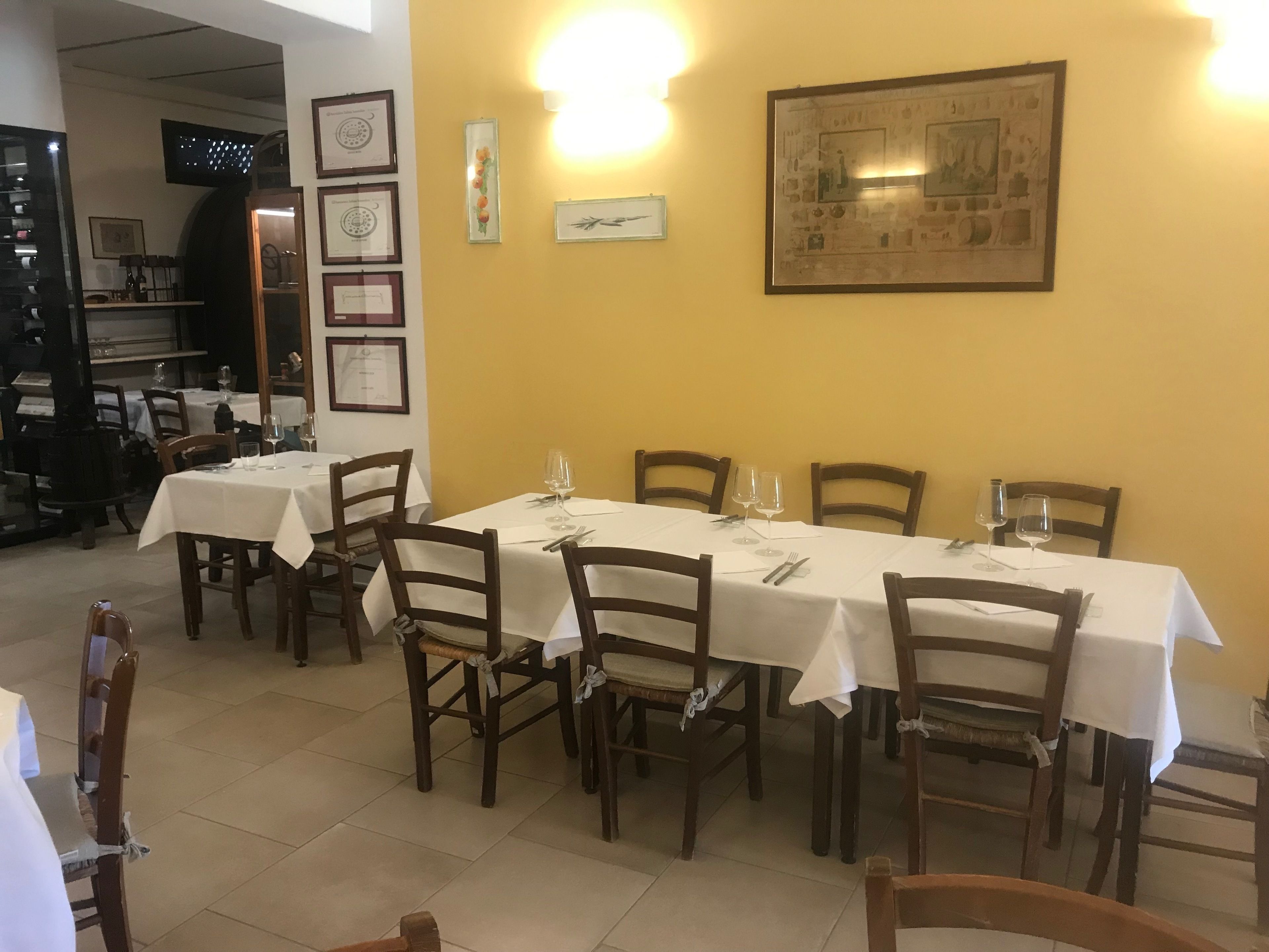 A dining area with tables set for four, wooden chairs, and framed artwork on the walls.
