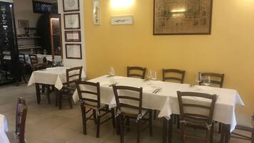 A dining area with tables set for four, wooden chairs, and framed artwork on the walls.