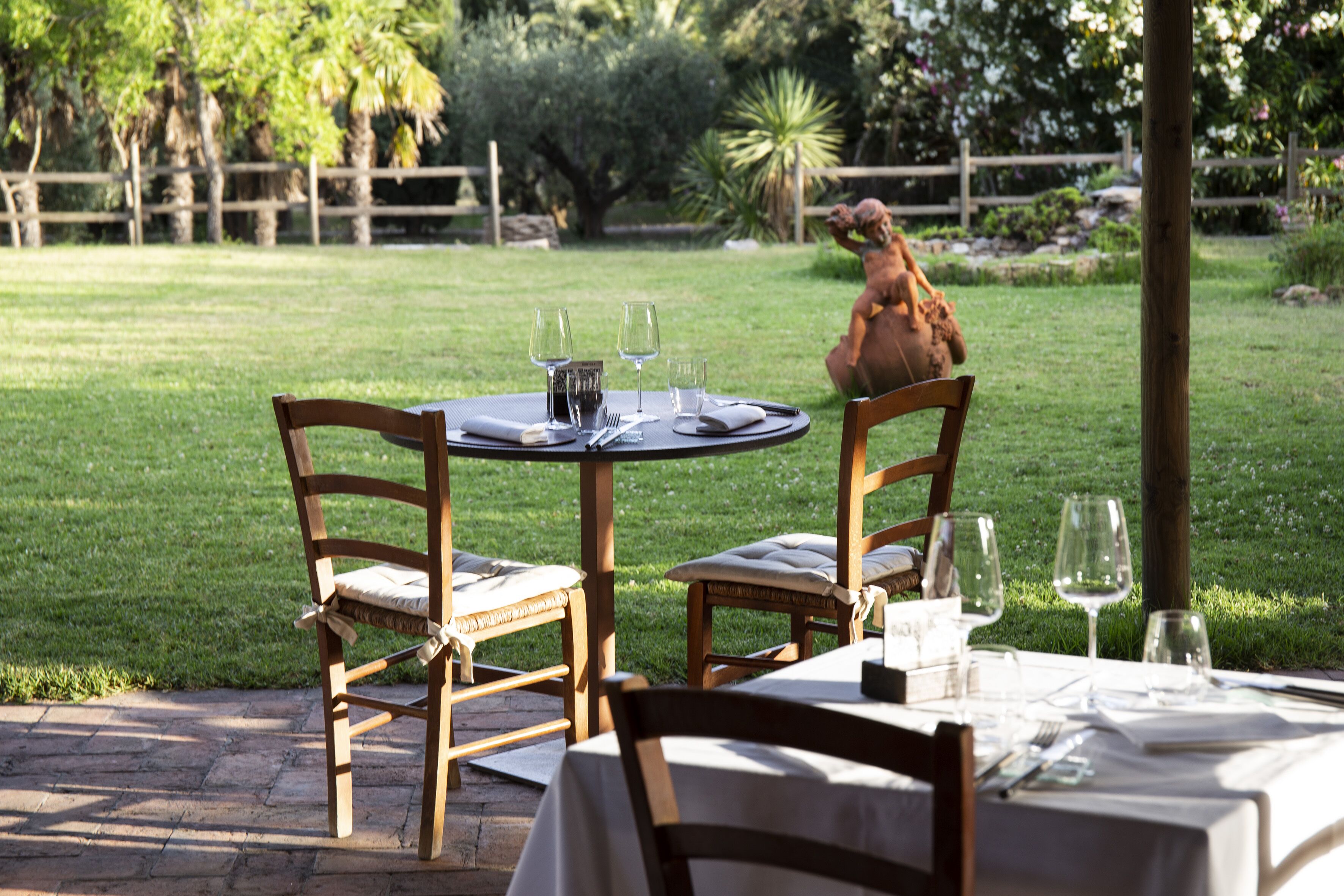 Una mesa de comedor al aire libre con sillas, una valla de madera y una estatua al fondo.