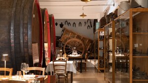 A restaurant with wooden tables and chairs, a large wooden wheel, and a glass display case with various items. - Azienda Agricola Sapereta (Porto Azzurro)