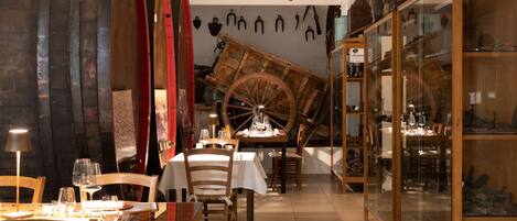 A restaurant with wooden tables and chairs, a large wooden wheel, and a glass display case with various items.