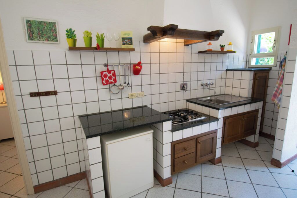 A kitchen with white tiled walls, a black countertop, a stove, and wooden cabinets.