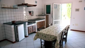 A kitchen with a tiled backsplash, a stove, a sink, and a dining table with chairs.