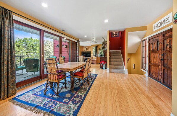 A spacious living area with a wooden dining table, chairs, and a large window overlooking a garden. - Luxury Riverfront Paradise Escape (Three Rivers)