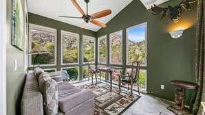 A sunroom with a large window, a ceiling fan, a sofa, a table, and chairs. - Luxury Riverfront Paradise Escape (Three Rivers)