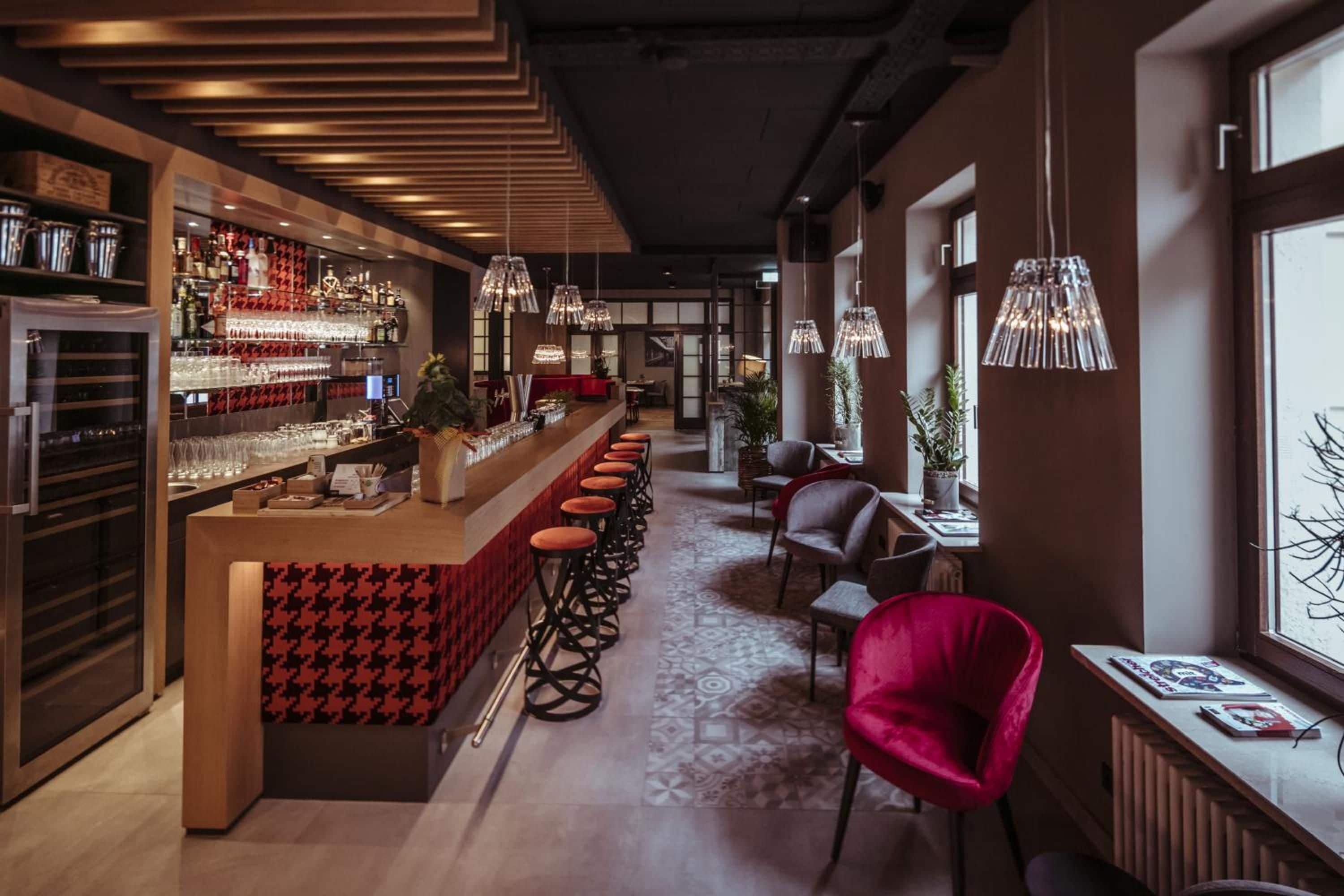 Una zona de bar con una barra alargada, taburetes y lámparas colgantes.