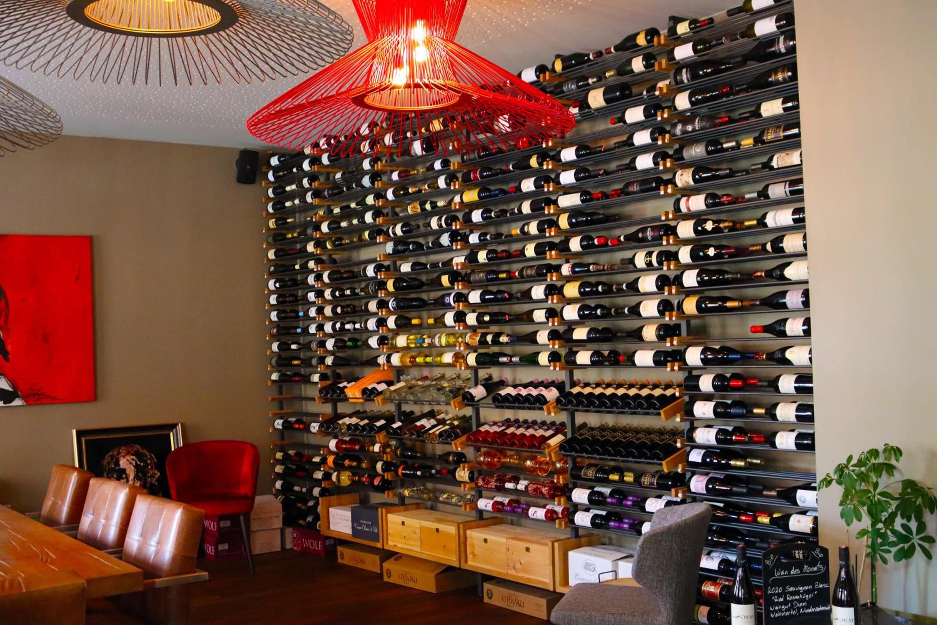 Una bodega con numerosas botellas organizadas en estantes, una silla roja, cajas de madera y una mesa con sillas.