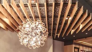 A modern reception area with a wooden ceiling design, a central chandelier, and a marble counter displaying the logo 'Anders Gastgeber'. - Alexxanders Restaurant & Bordinghouse (Chemnitz)