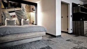 A modern bedroom with a large bed, a stone wall mural, and a staircase. - Alexxanders Restaurant & Bordinghouse (Chemnitz)