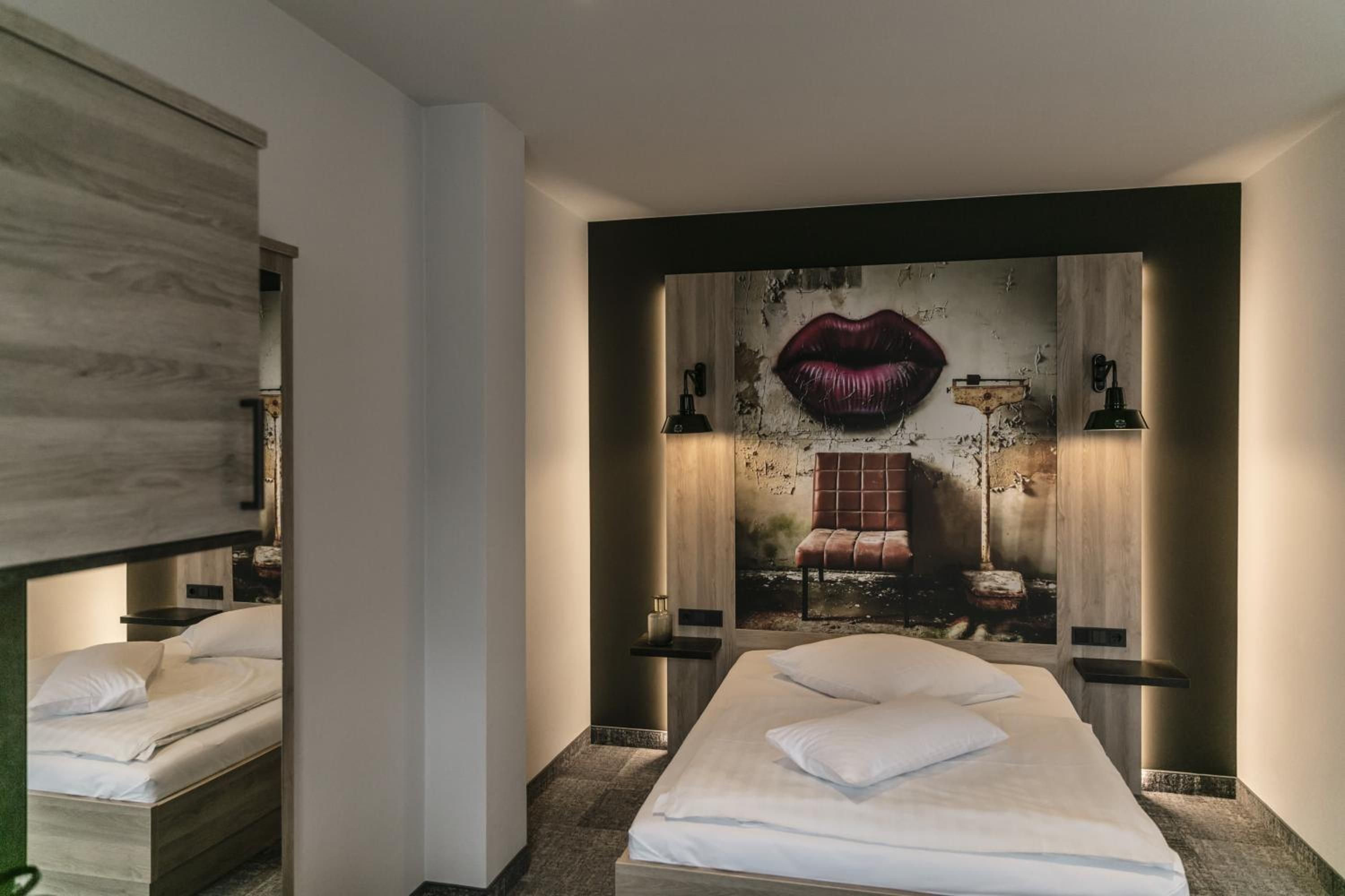 Een hotelkamer met een groot bed, twee nachtkastjes, een spiegel en een wanddecoratie van lippen.