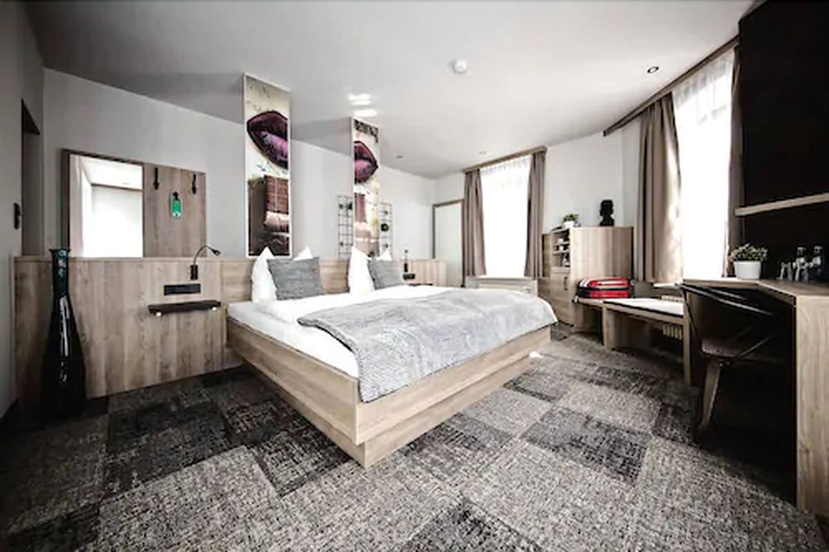 A modern hotel room with a large bed, a desk, and a wardrobe.