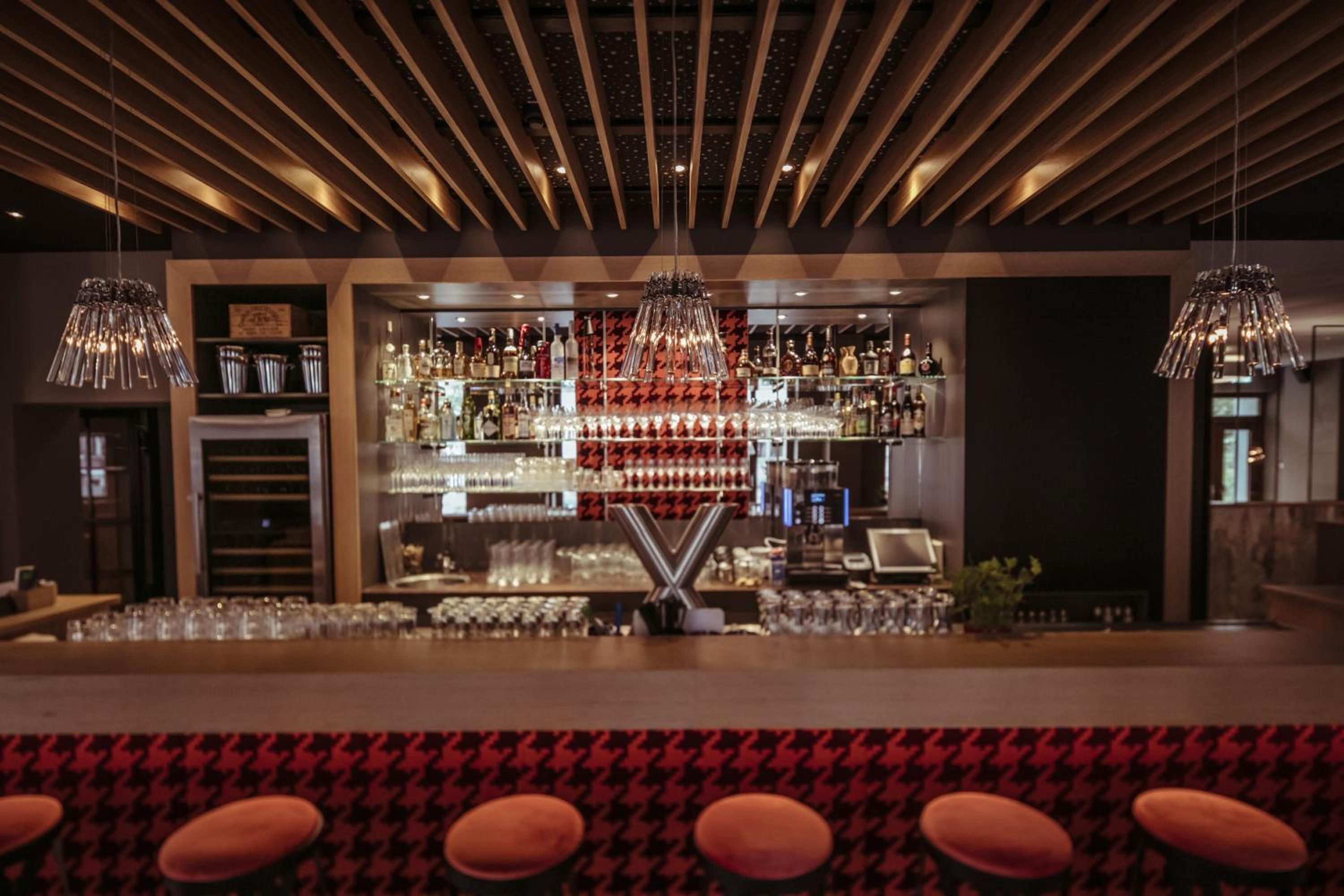 Eine Bar mit modernem Design, inklusive einer Theke mit Hockern, einer Auswahl an Flaschen und Gläsern sowie hängenden Leuchten.
