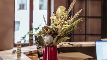 Ein Empfangsbereich mit einem roten Blumenstrauß in einer Vase, einer modernen Kronleuchter und einem Bildschirm.
