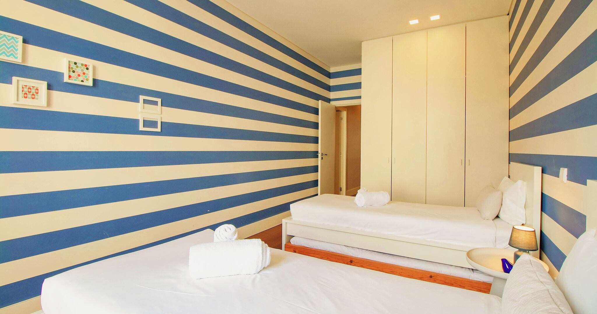 A hotel room with striped walls, a bed, a nightstand, and a wardrobe.