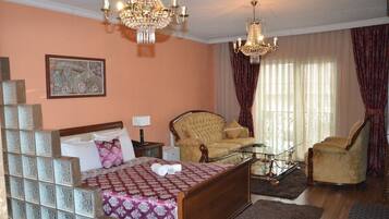 A hotel room with a bed, a sofa, a glass coffee table, and two armchairs.